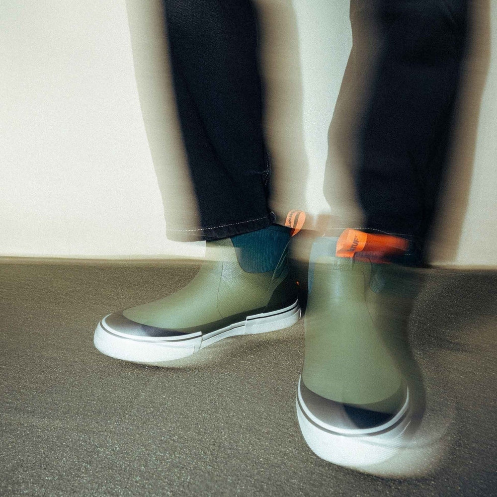Olive green Out of the Ordinary Ankle Deck Boots with white soles and orange pull tabs, worn with dark pants.